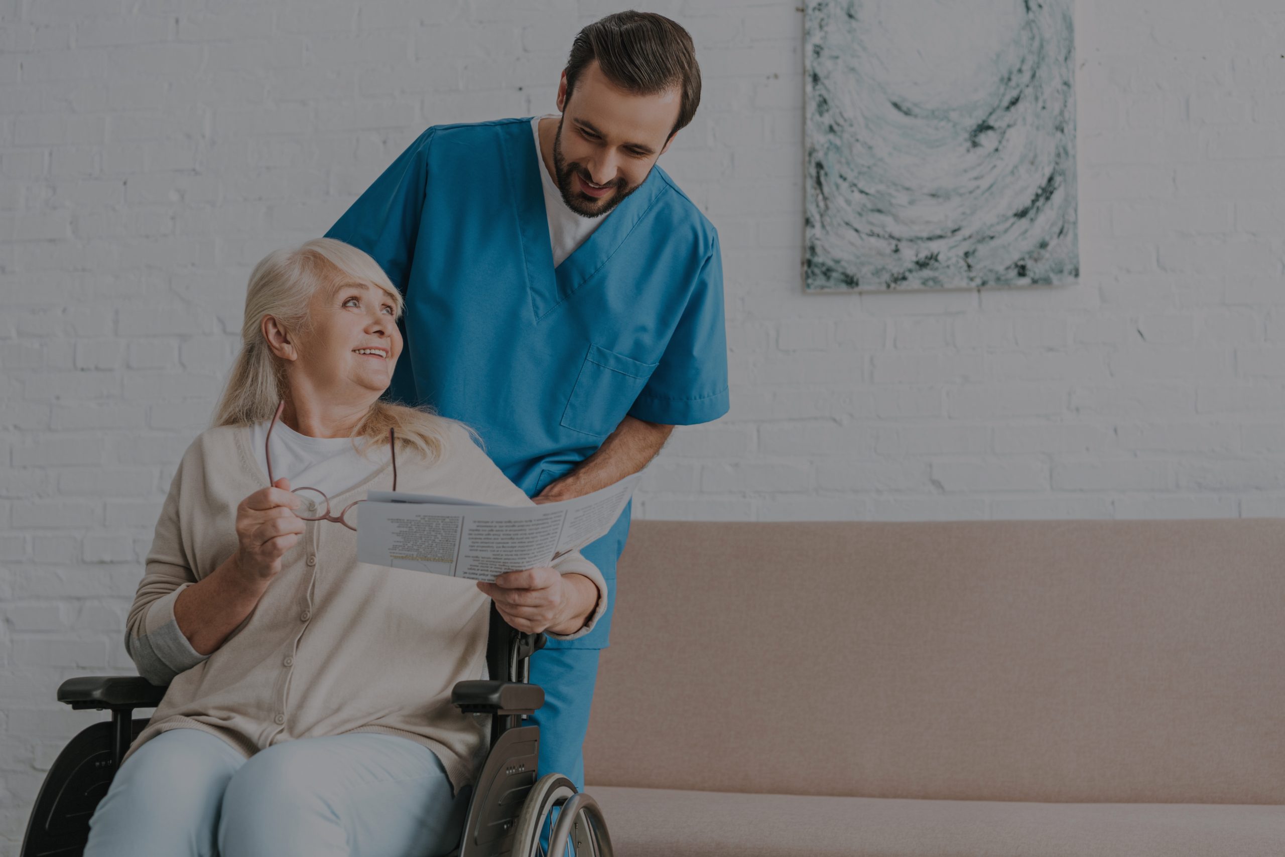 smiling young male nurse looking at happy senior woman reading n